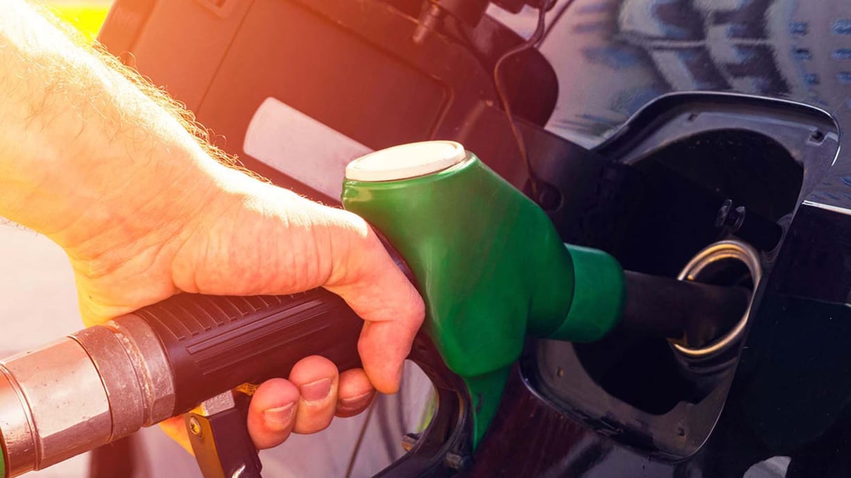 Hand hält grüne Zapfpistole am Tankstutzen eines dunklen Fahrzeugs beim Betanken.