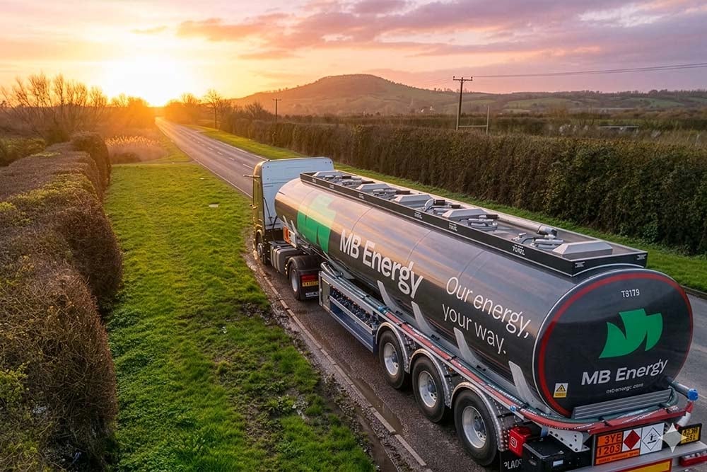 MB-Energy-Tankwagen fährt bei Sonnenaufgang auf einer Landstraße durch grüne Felder.